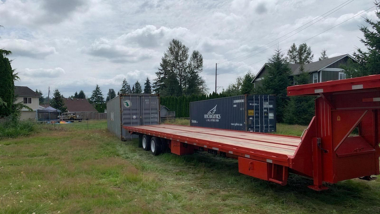 gooseneck tilt-bed trailer delivering a shipping container to a Kansas City property